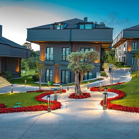 Menalo Hotel Premium Istanbul Airport Exterior photo The photo depicts a scenic outdoor area in a modern residential or resort setting. There are contemporary buildings with multiple levels and large windows. The landscape features a well-maintained pathway that is illuminated, leading through a garden