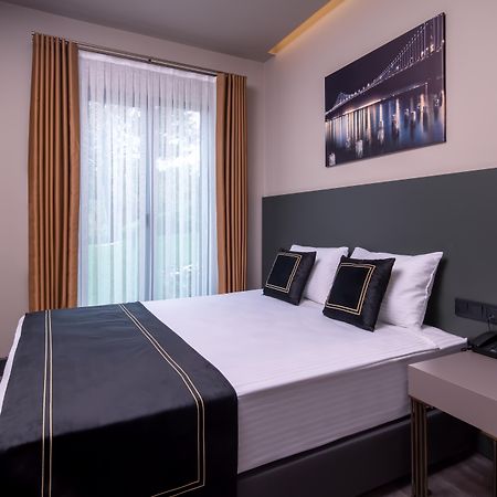 Menalo Hotel Premium Istanbul Airport Exterior photo The photo shows a modern hotel room featuring a double bed with a sleek black and white bedding set. Two decorative pillows are placed on the bed. There are large windows with sheer curtains that allow natural light to enter the room, and the walls a
