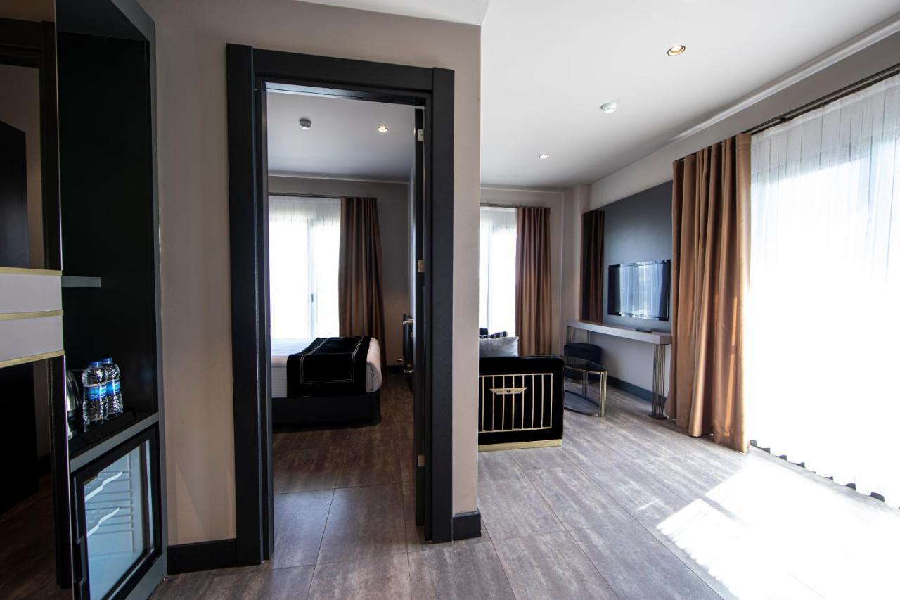 Menalo Hotel Premium Istanbul Airport Exterior photo The photo shows an interior space, likely a hotel room or a suite. It features a doorway leading to another room, with light-colored walls and wooden floors. On the left, there is a mini-fridge with drinks, and in the main area, there are large windo