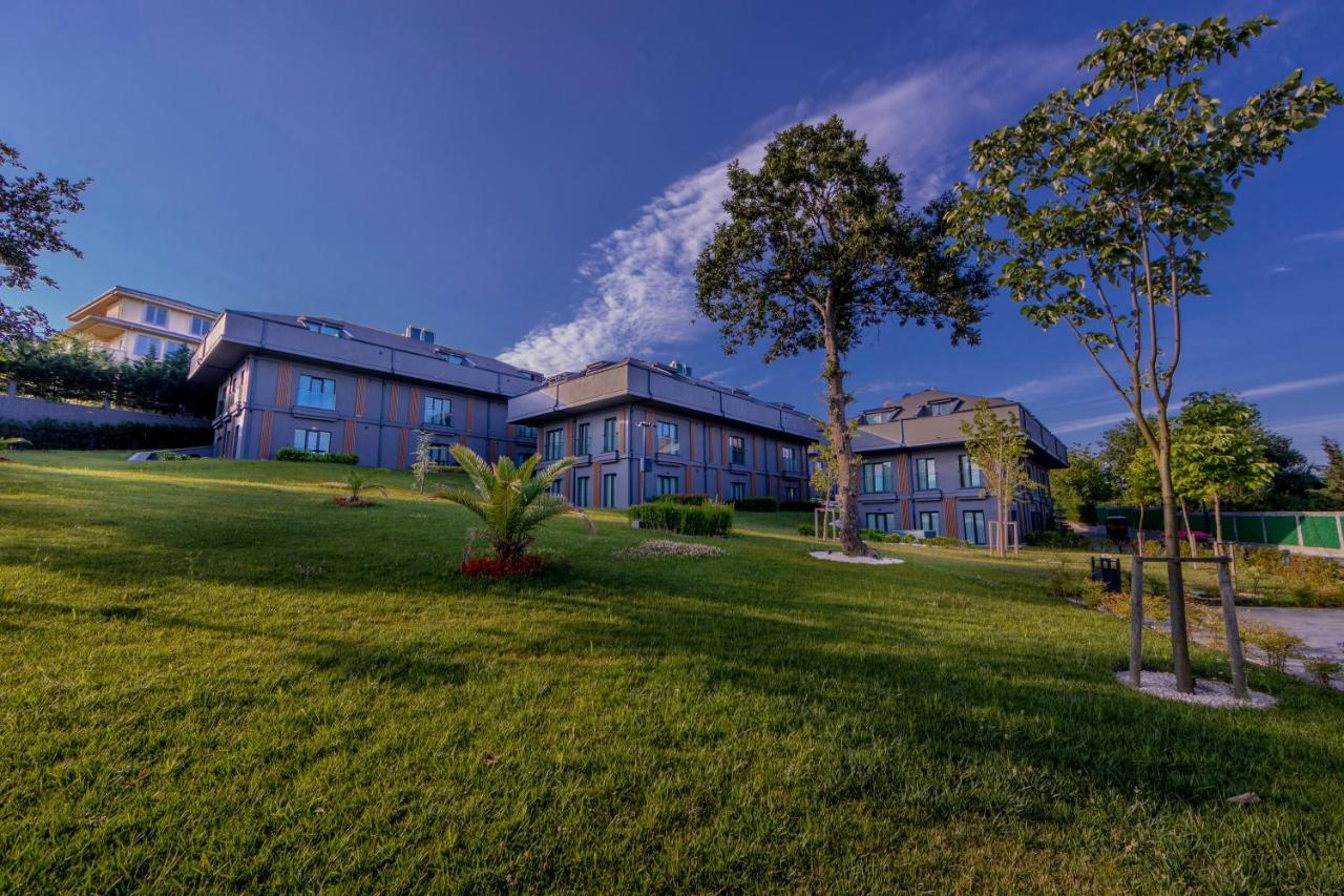 Menalo Hotel Premium Istanbul Airport Exterior photo The photo shows a picturesque landscape featuring a group of buildings situated on a grassy lawn. The buildings are modern in design and have large windows. They are surrounded by well-maintained greenery, including trees and ornamental plants. The s