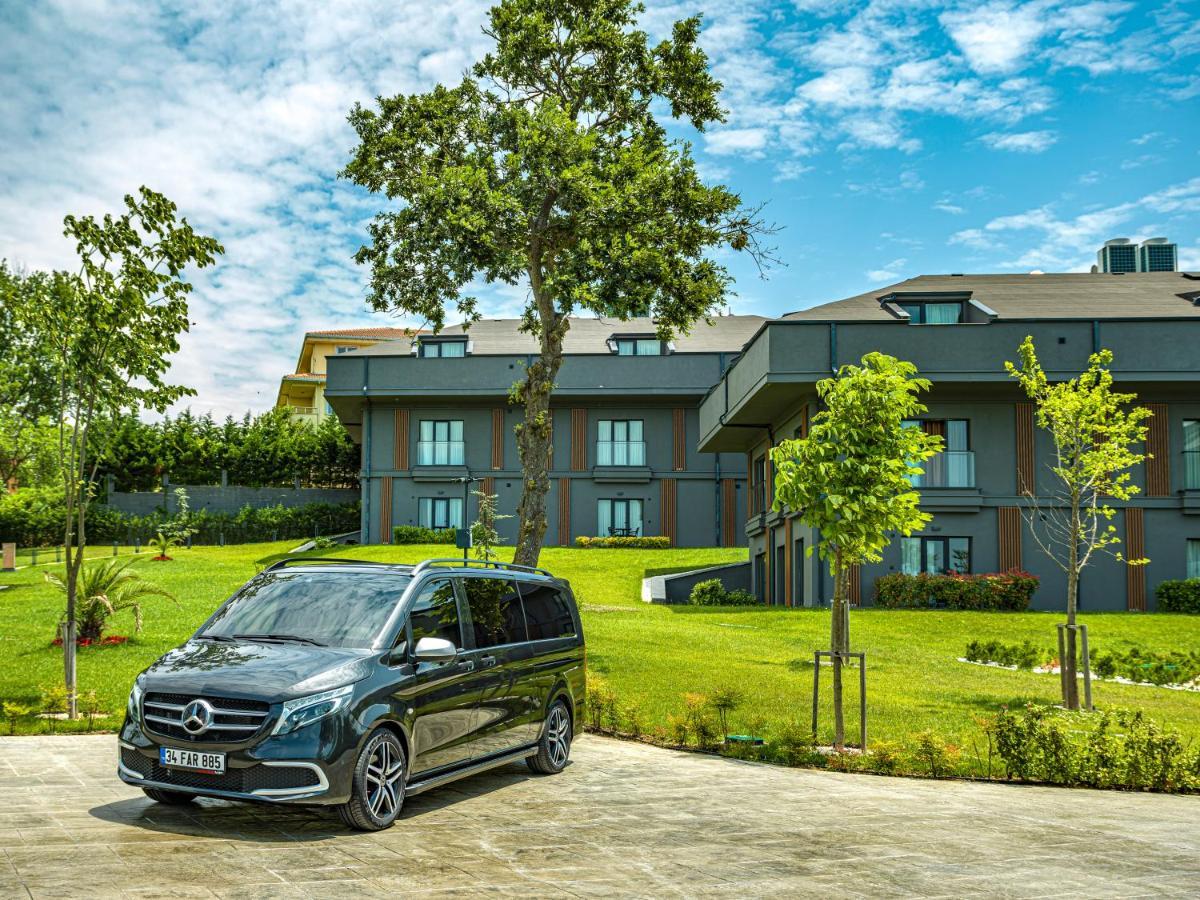 Menalo Hotel Premium Istanbul Airport Exterior photo The photo features a sleek black Mercedes van parked on a paved area in front of a modern building. The building appears to have multiple levels and large windows, surrounded by well-maintained green lawns and several young trees. The sky is partly c