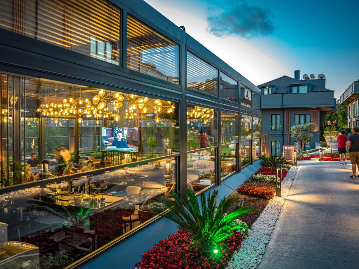 Menalo Hotel Premium Istanbul Airport Exterior photo The photo shows a modern restaurant with a glass facade, illuminated by warm lights that create a cozy atmosphere. The interior appears vibrant, with diners enjoying their meals. Outside, there is a well-maintained pathway lined with decorative plant