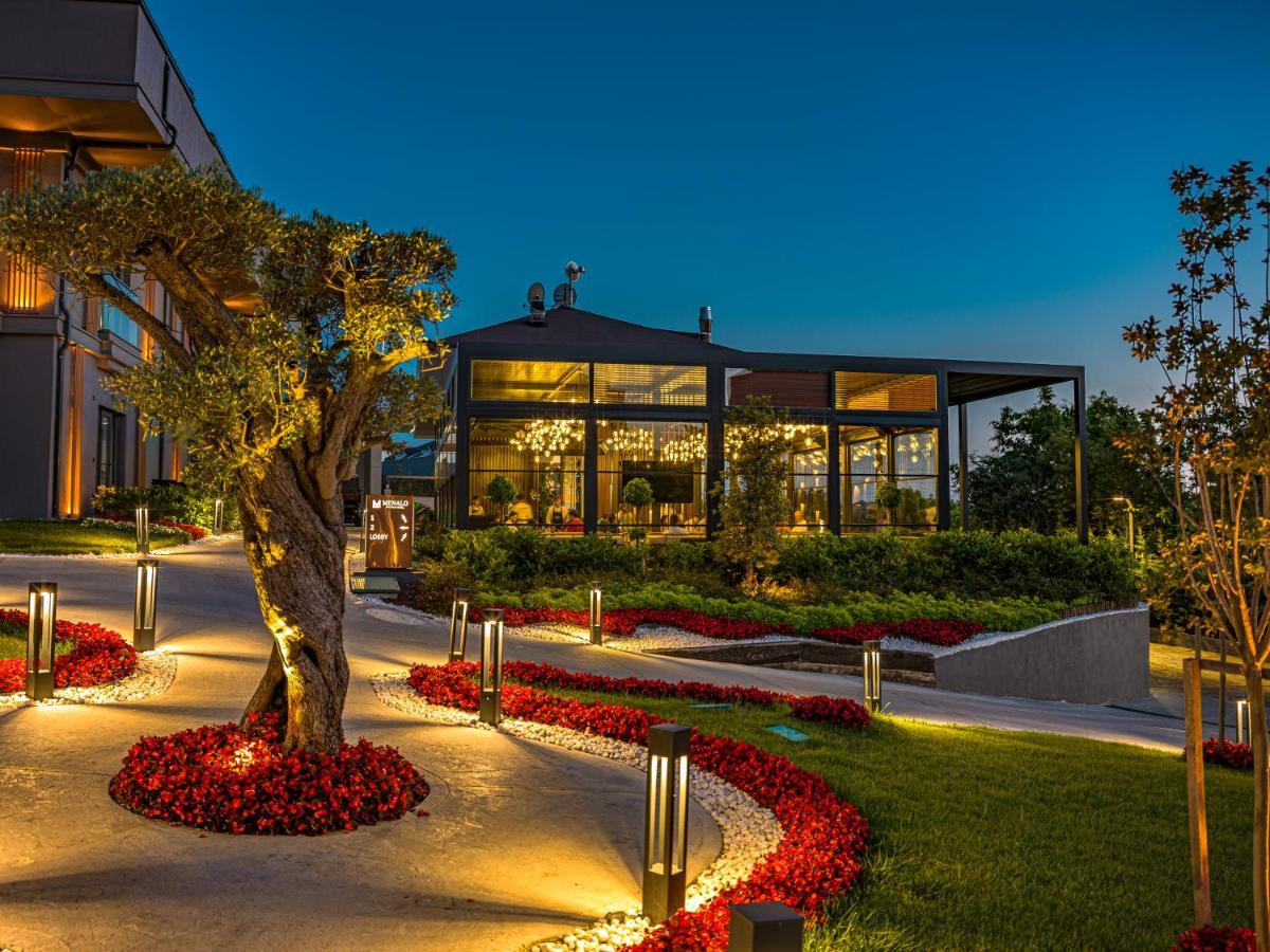 Menalo Hotel Premium Istanbul Airport Exterior photo The photo shows a beautifully landscaped outdoor area of a restaurant or cafe. The scene is set during twilight, with the sky gradually darkening. 

In the foreground, there is a curved pathway illuminated by modern light fixtures and bordered by vib