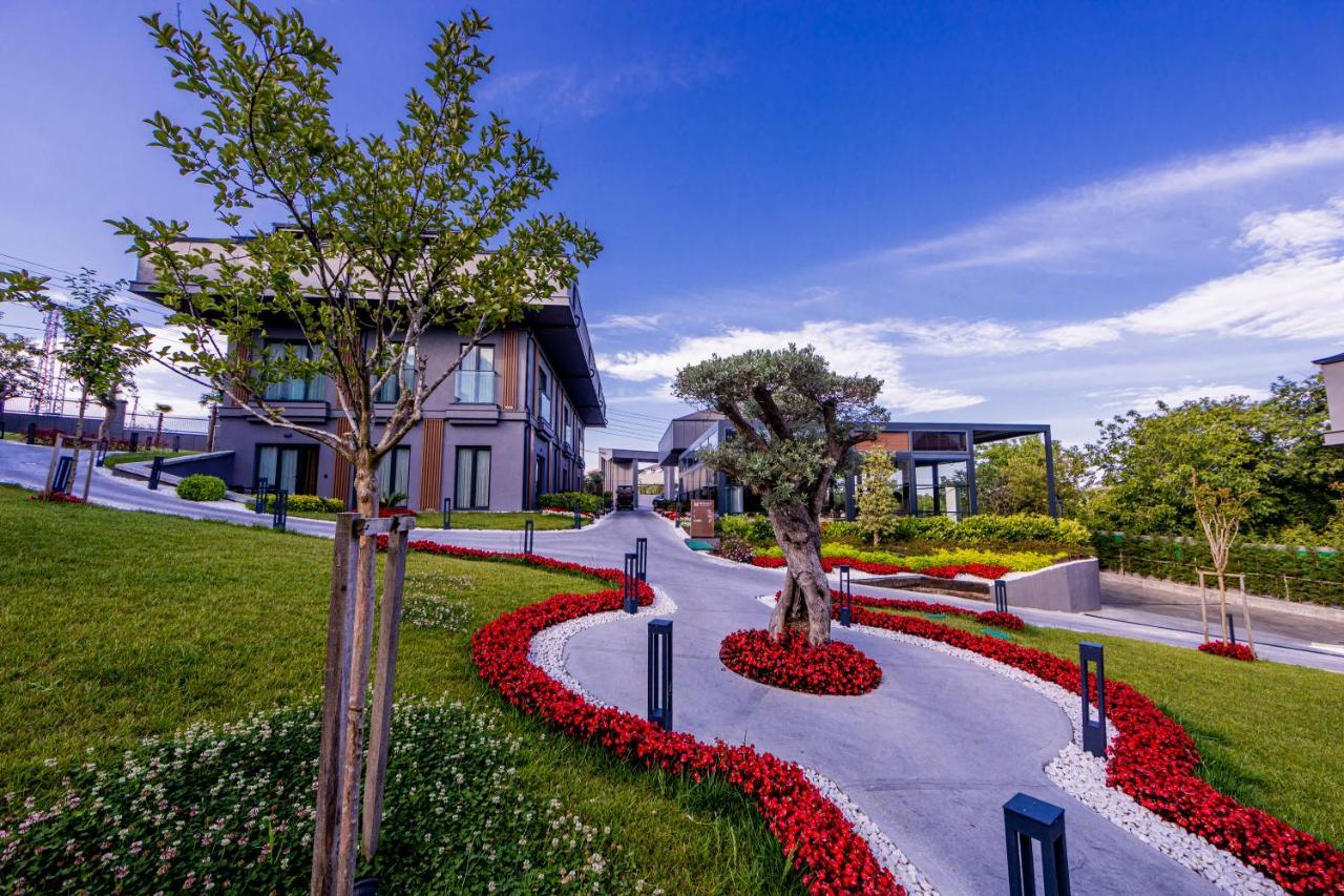 Menalo Hotel Premium Istanbul Airport Exterior photo The photo depicts a beautifully landscaped area featuring modern architecture. There are several contemporary-style buildings set against a backdrop of clear blue skies. The landscape is designed with neatly manicured grass and vibrant flower beds, p