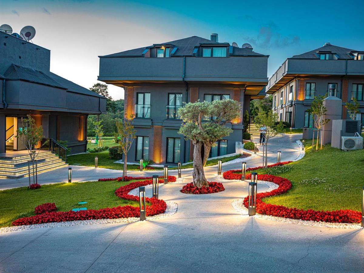 Menalo Hotel Premium Istanbul Airport Exterior photo The photo depicts a scenic outdoor area in a modern residential or resort setting. There are contemporary buildings with multiple levels and large windows. The landscape features a well-maintained pathway that is illuminated, leading through a garden