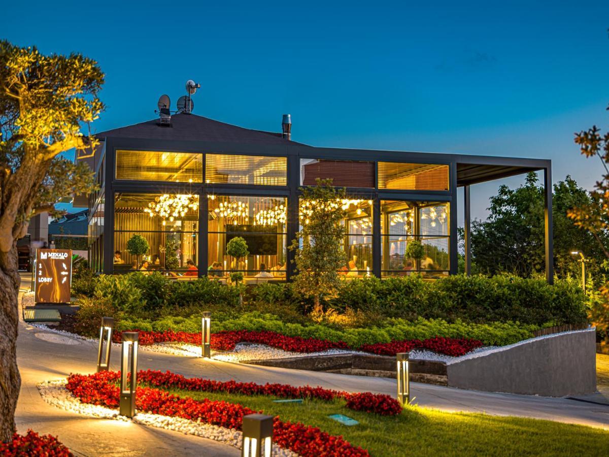 Menalo Hotel Premium Istanbul Airport Exterior photo The photo shows a modern restaurant or café building set against a twilight backdrop. The structure features large glass windows and an elegant design, allowing for visibility of the interior and the lighting within. Surrounding the building, there i