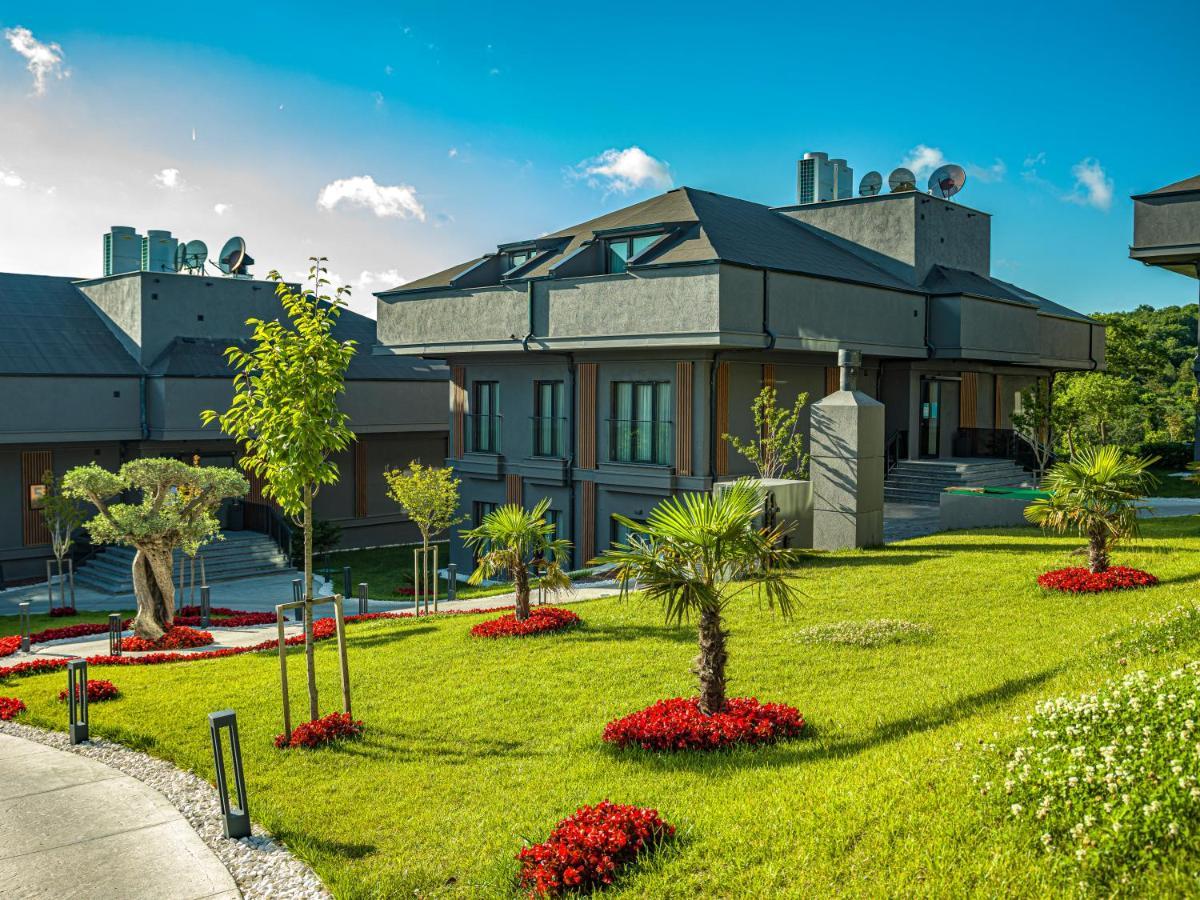 Menalo Hotel Premium Istanbul Airport Exterior photo The photo shows a modern residential area featuring several contemporary houses. The buildings have a sleek, architectural design with flat roofs and large windows. Surrounding the houses is a well-maintained lawn adorned with vibrant flower beds, pr