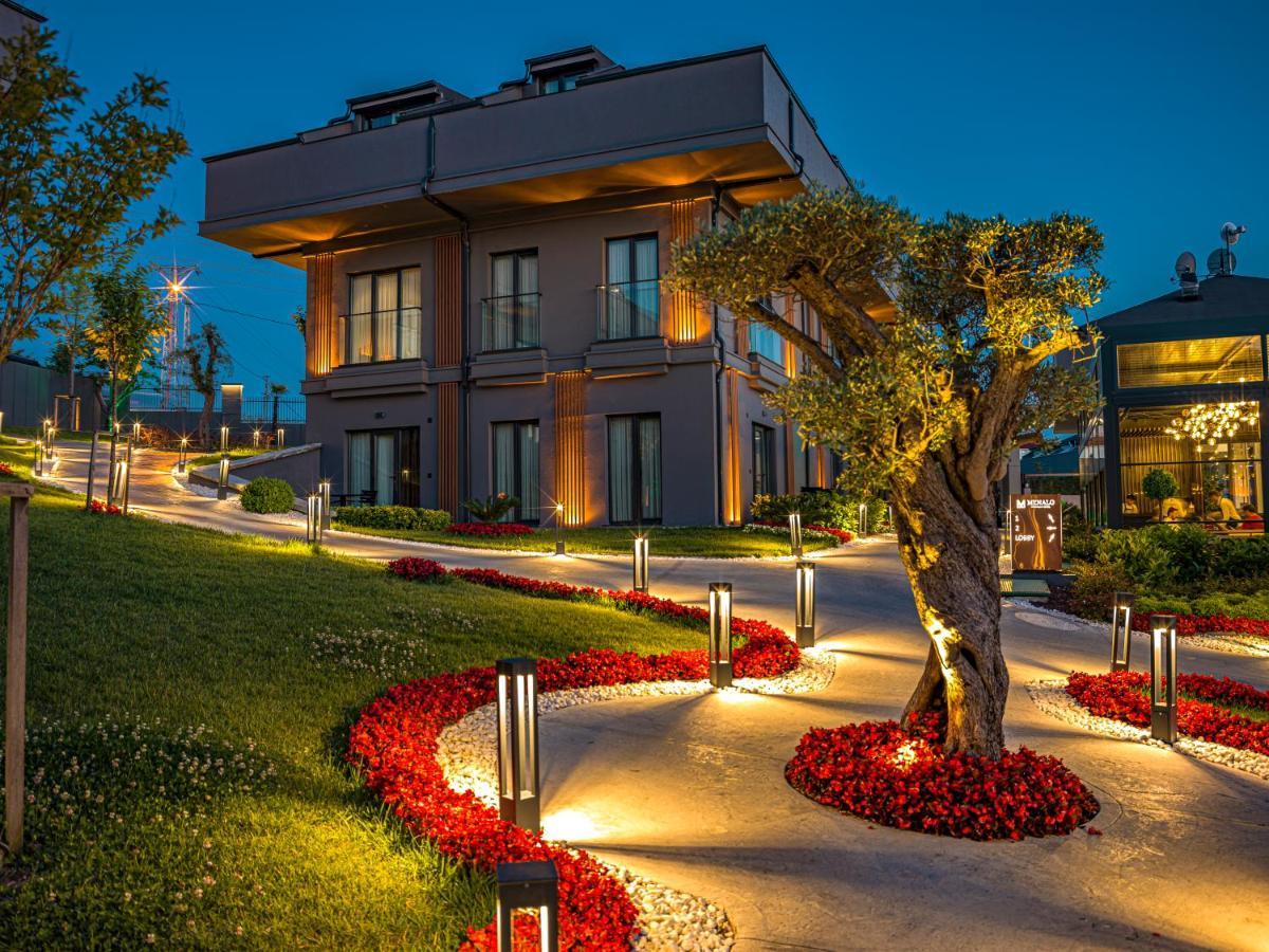 Menalo Hotel Premium Istanbul Airport Exterior photo The photo depicts a beautiful outdoor scene during the evening, featuring a modern building. The building has multiple stories and large windows, illuminated softly by outdoor lighting. Surrounding the building is a landscaped area with a winding pat
