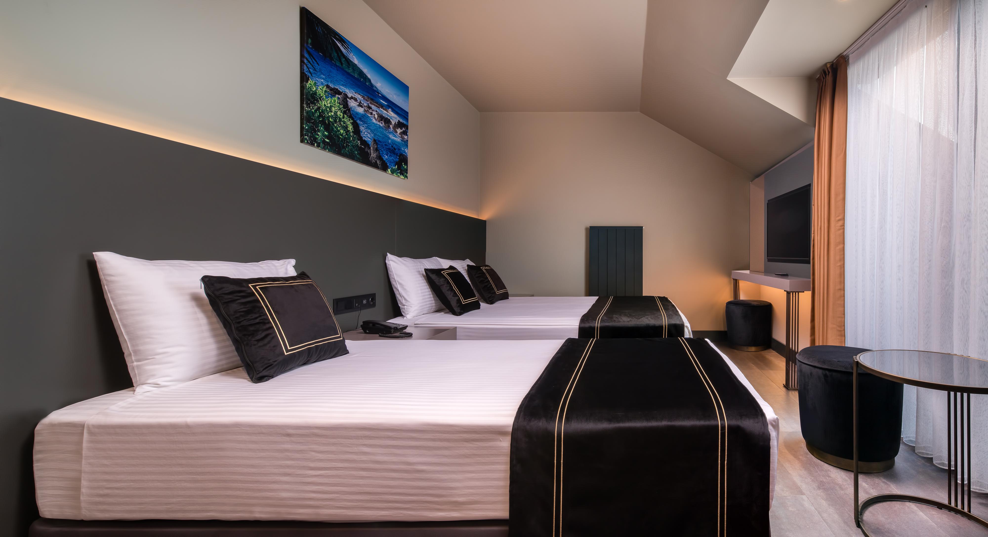 Menalo Hotel Premium Istanbul Airport Exterior photo The photo depicts a modern hotel room featuring two beds with white linens and black decorative elements, such as pillows and bed runners. The room has a minimalist design with a dark accent wall and soft ambient lighting. A mounted television is vis