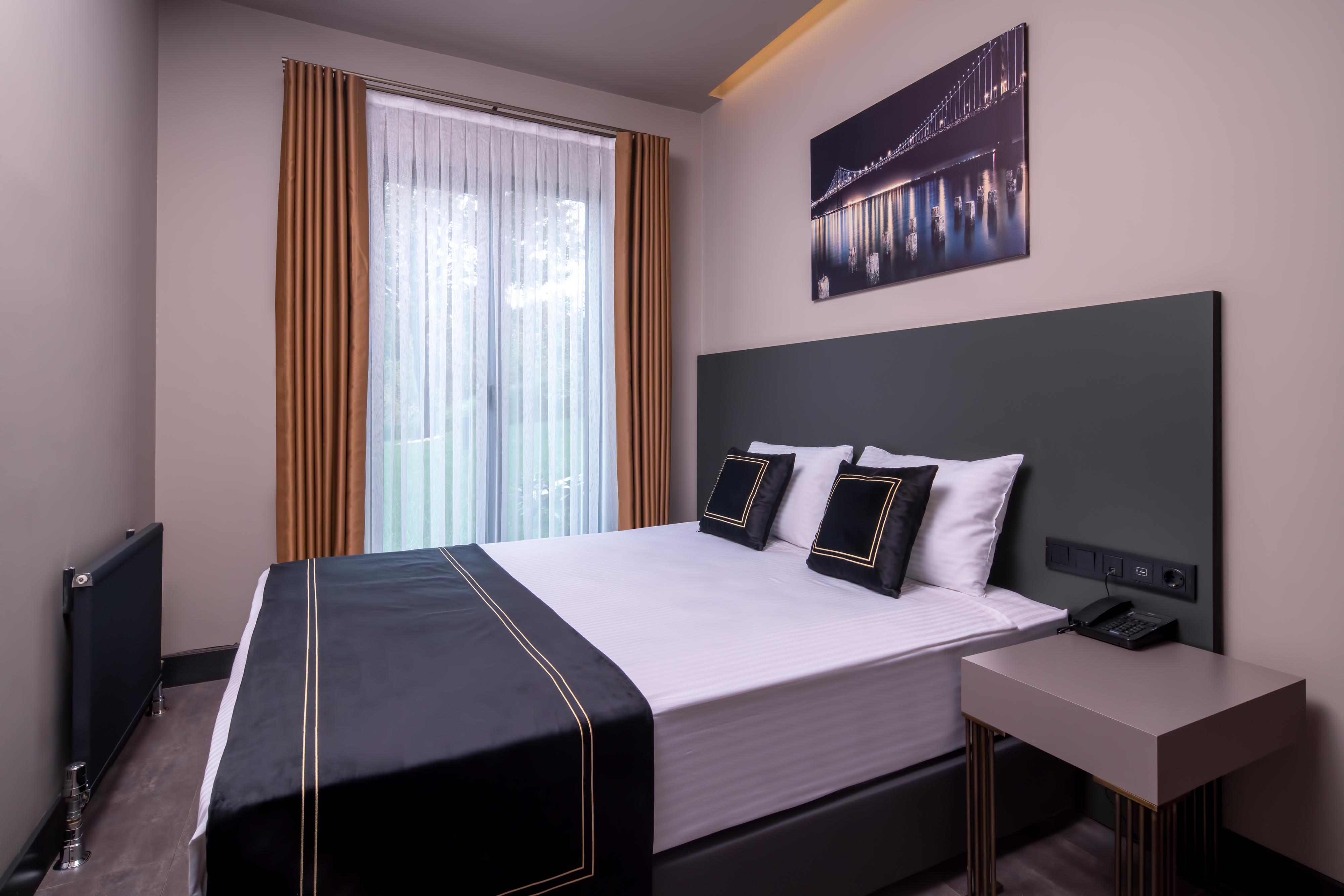 Menalo Hotel Premium Istanbul Airport Exterior photo The photo shows a modern hotel room featuring a double bed with a sleek black and white bedding set. Two decorative pillows are placed on the bed. There are large windows with sheer curtains that allow natural light to enter the room, and the walls a