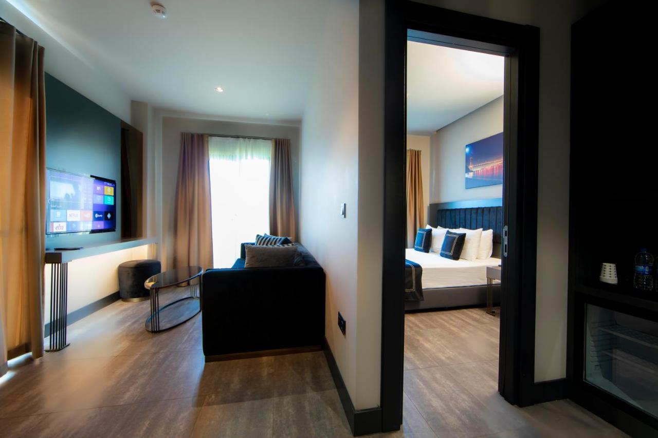 Menalo Hotel Premium Istanbul Airport Exterior photo The photo shows an interior space, likely a hotel suite or an apartment. On the left, there is a small living area with a couch and a wall-mounted television. There are large windows with curtains allowing natural light to enter. On the right, there 