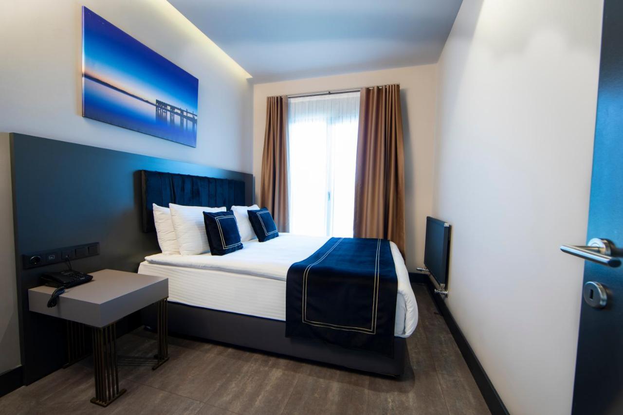 Menalo Hotel Premium Istanbul Airport Exterior photo The photo shows a modern hotel room featuring a double bed with white linens and dark blue decorative pillows. The walls are painted in neutral tones, and there is a large piece of artwork depicting a serene landscape above the bed. Natural light ent