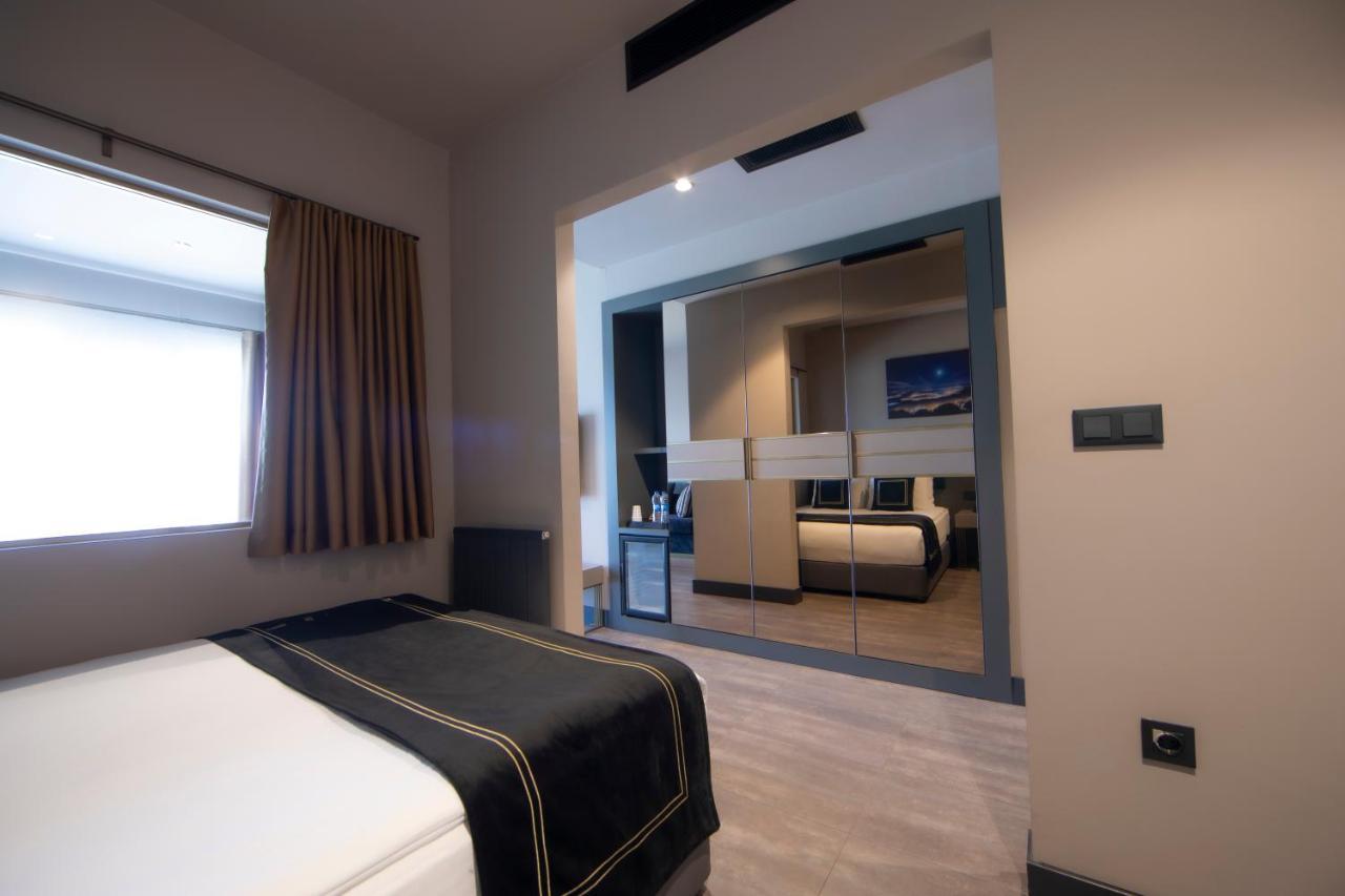 Menalo Hotel Premium Istanbul Airport Exterior photo The photo shows a modern hotel room or guest room. In the foreground, there is a bed with a white mattress and a dark-colored throw blanket, suggesting a neat and elegant setting. The walls are light-colored, which adds to the contemporary feel. 

To