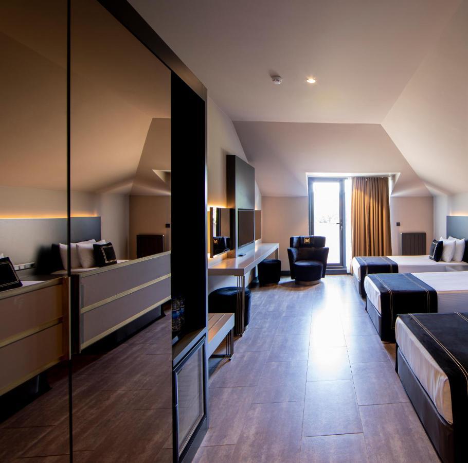 Menalo Hotel Premium Istanbul Airport Exterior photo The photo shows a modern hotel room with a sleek design. It features two beds with dark bedding, a large mirror reflecting the space, and a comfortable seating area with a chair. There is a desk against the wall, and the room has a large window with 