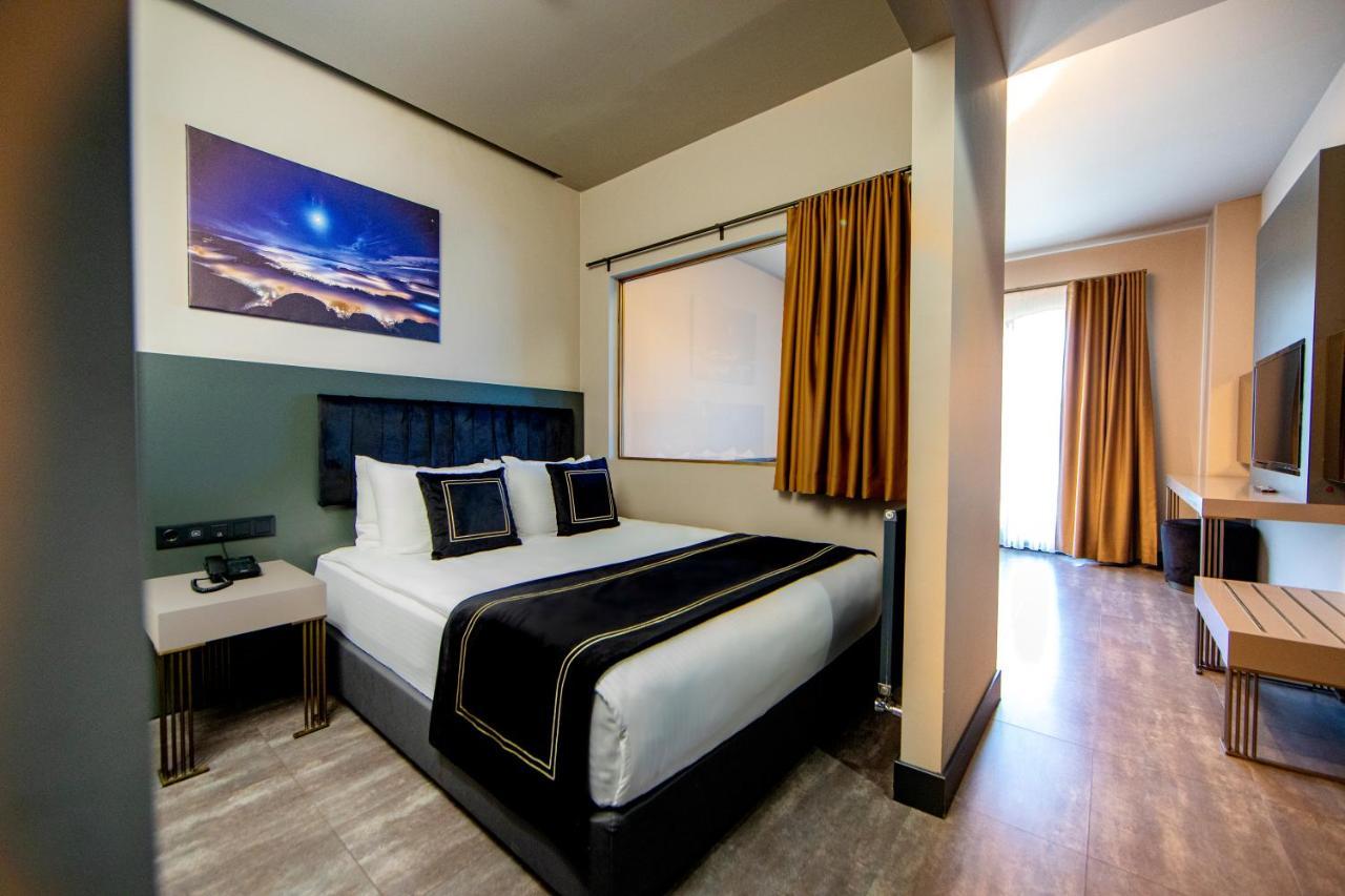 Menalo Hotel Premium Istanbul Airport Exterior photo The photo shows a modern hotel room featuring a bed with crisp white and black bedding. There are two decorative pillows on the bed, and a piece of art is displayed above it, depicting a scenic landscape with a night sky. The room has a window with n