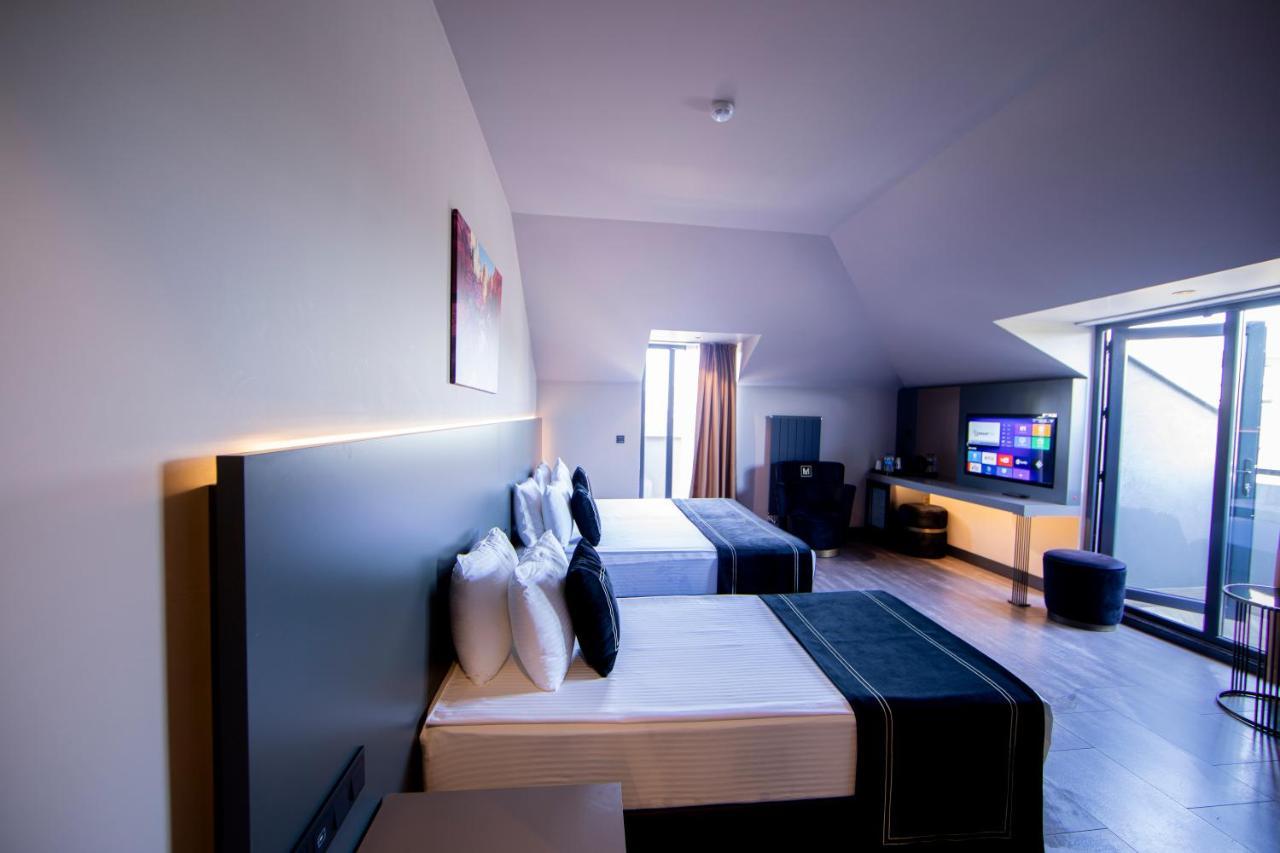 Menalo Hotel Premium Istanbul Airport Exterior photo The photo shows a modern hotel room featuring two beds with stylish black and white bedding. Each bed is adorned with several white pillows. The room has a contemporary design with a light-colored wall and hardwood flooring. There is a large window a